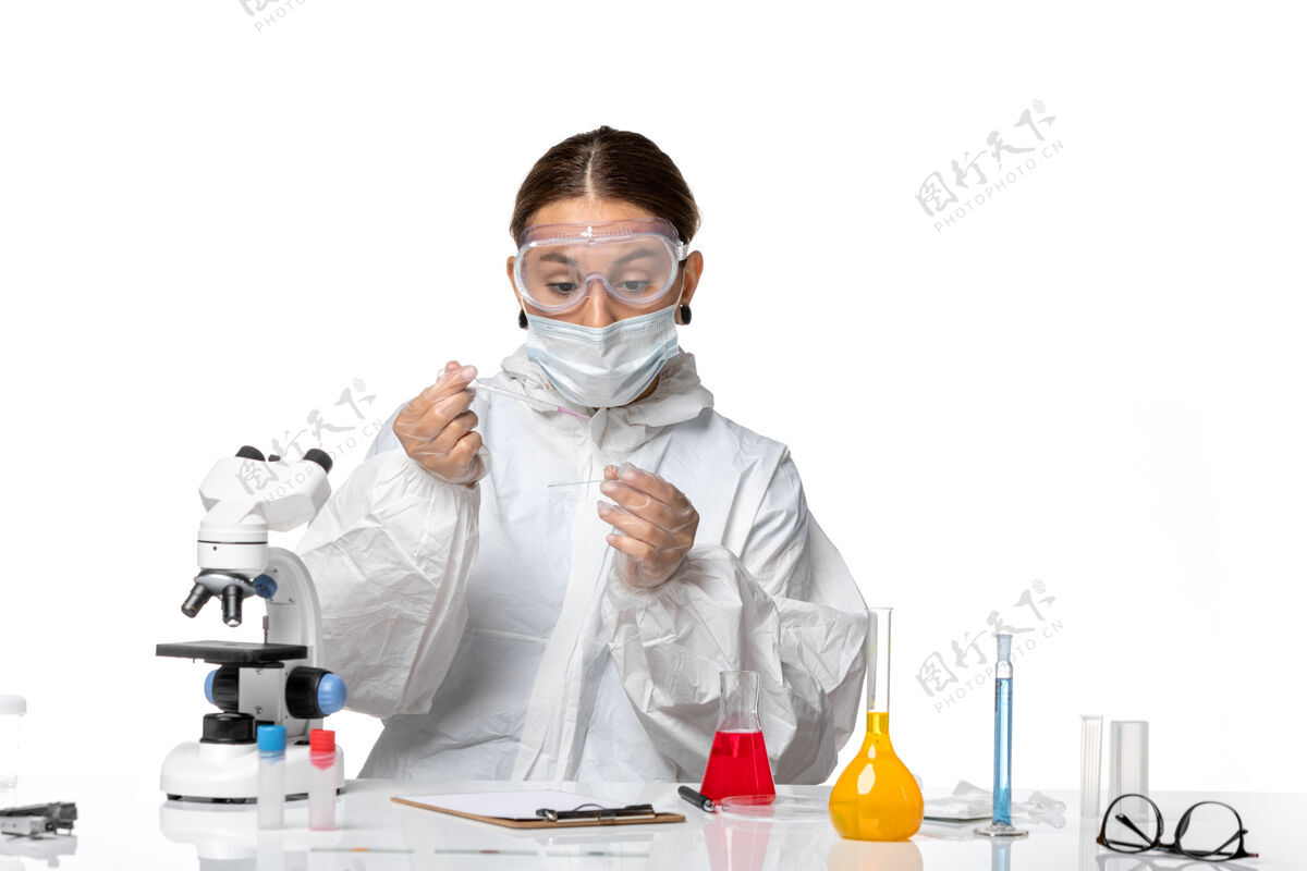 正面前视图穿着防护服 戴着口罩的女医生正在用白色背景病毒大流行冠状病毒的溶液工作医疗药物医生