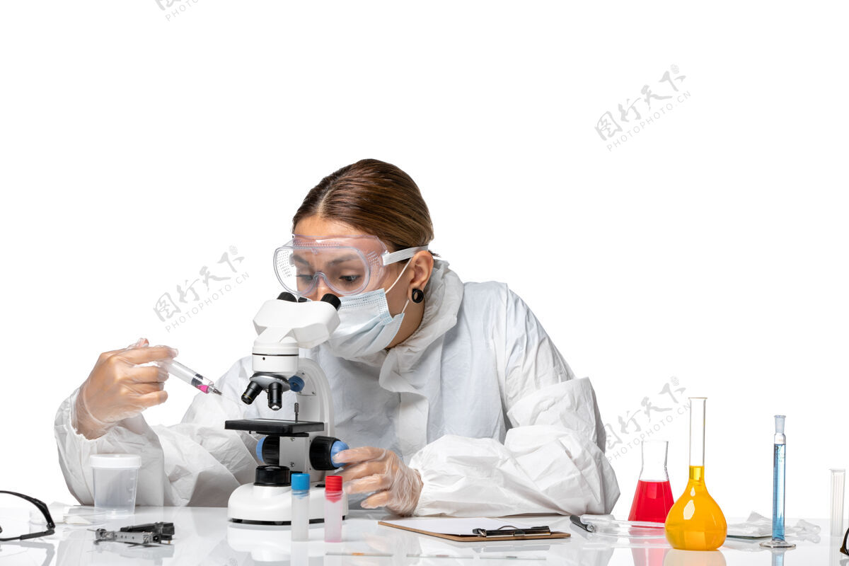 面罩正面图女医生穿着防护服 戴着口罩 用显微镜观察背景为浅白色的健康冠状病毒大流行女医生实验室外套