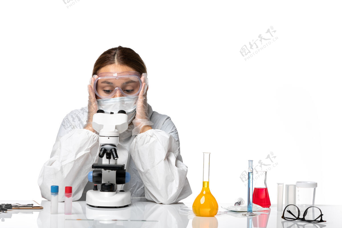 女医生前视图女医生穿着特制的工作服 戴着口罩 用显微镜观察浅白色背景的冠状病毒大流行显微镜正面医生