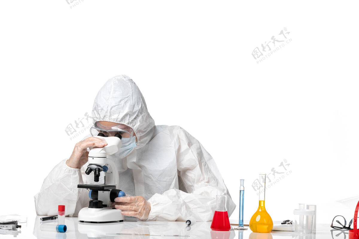 喷溅前视图：女医生穿着防护服 戴着口罩 在白色背景下使用显微镜观察病毒大流行 溅起病毒套装显微镜人