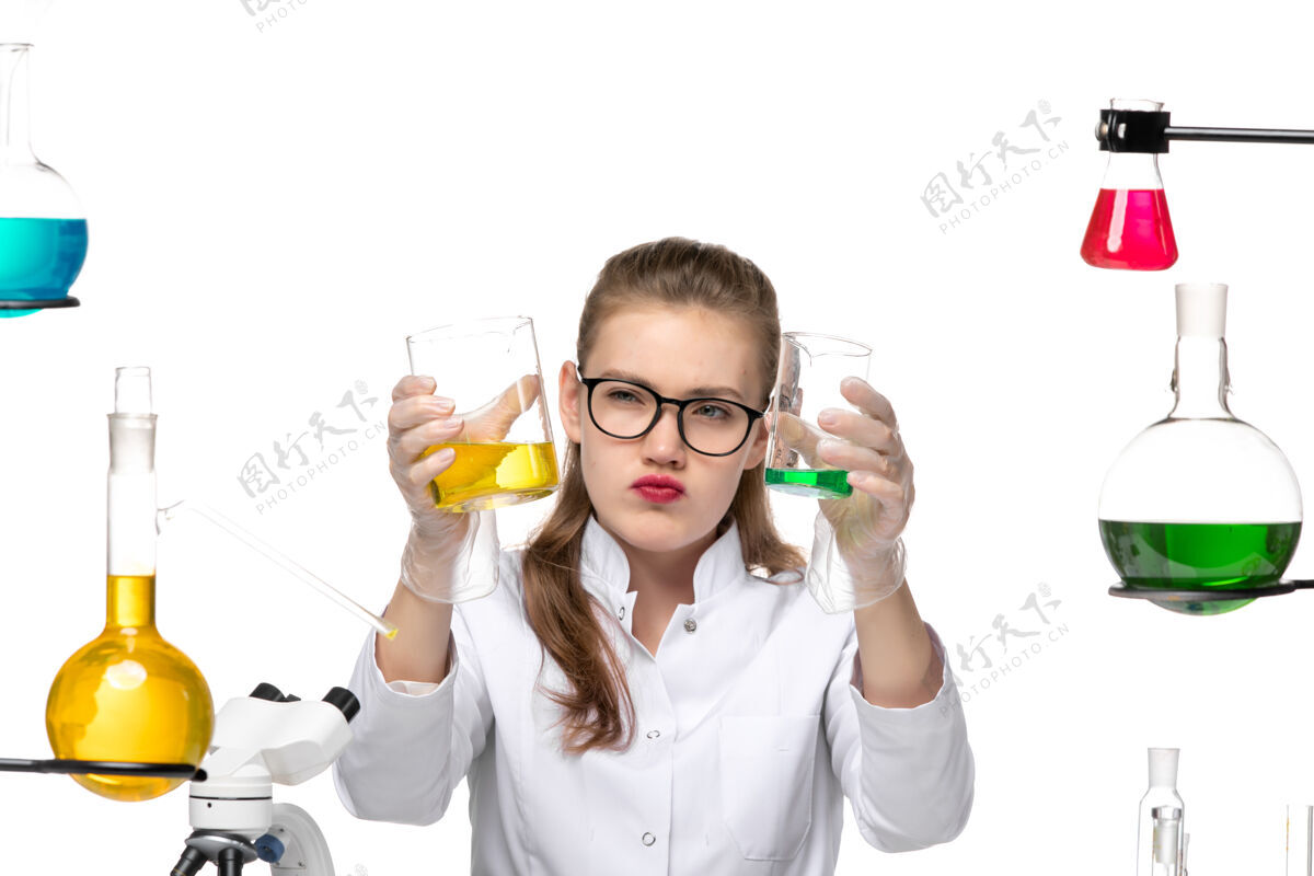健康正面近距离观察穿着医疗服的女化学家拿着装有白色背景化学大流行健康病毒溶液的烧瓶手持面部化学