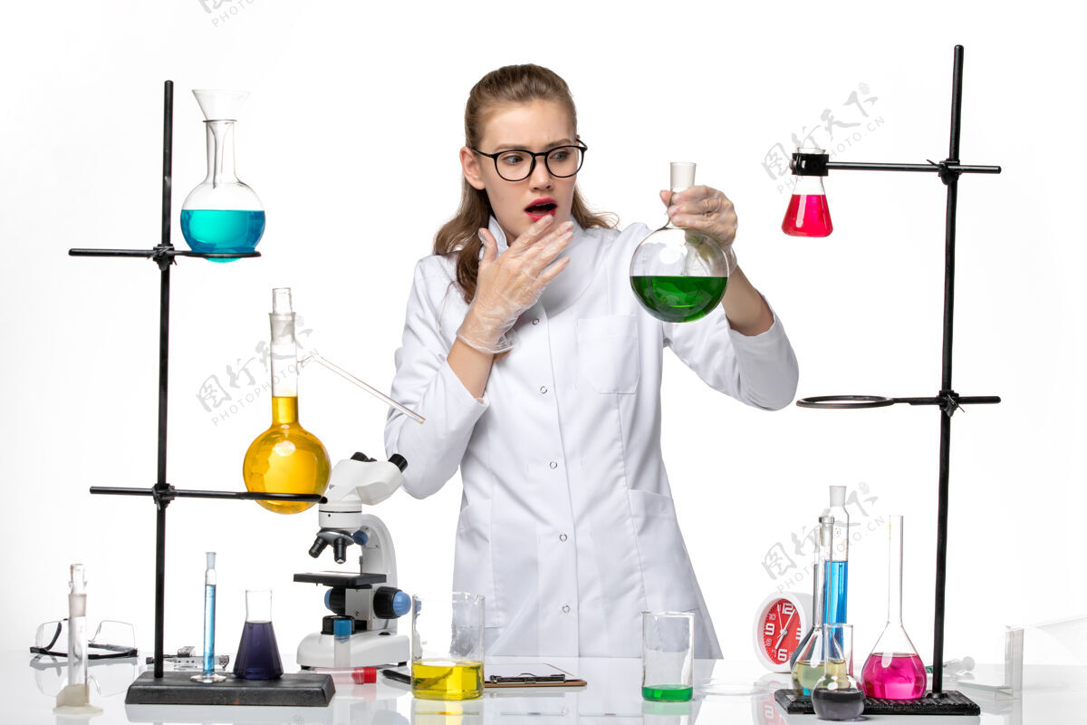 实验室前视图穿着医疗服的女化学家拿着白色背景上带绿色溶液的烧瓶化学大流行性冠状病毒瓶子前面医学