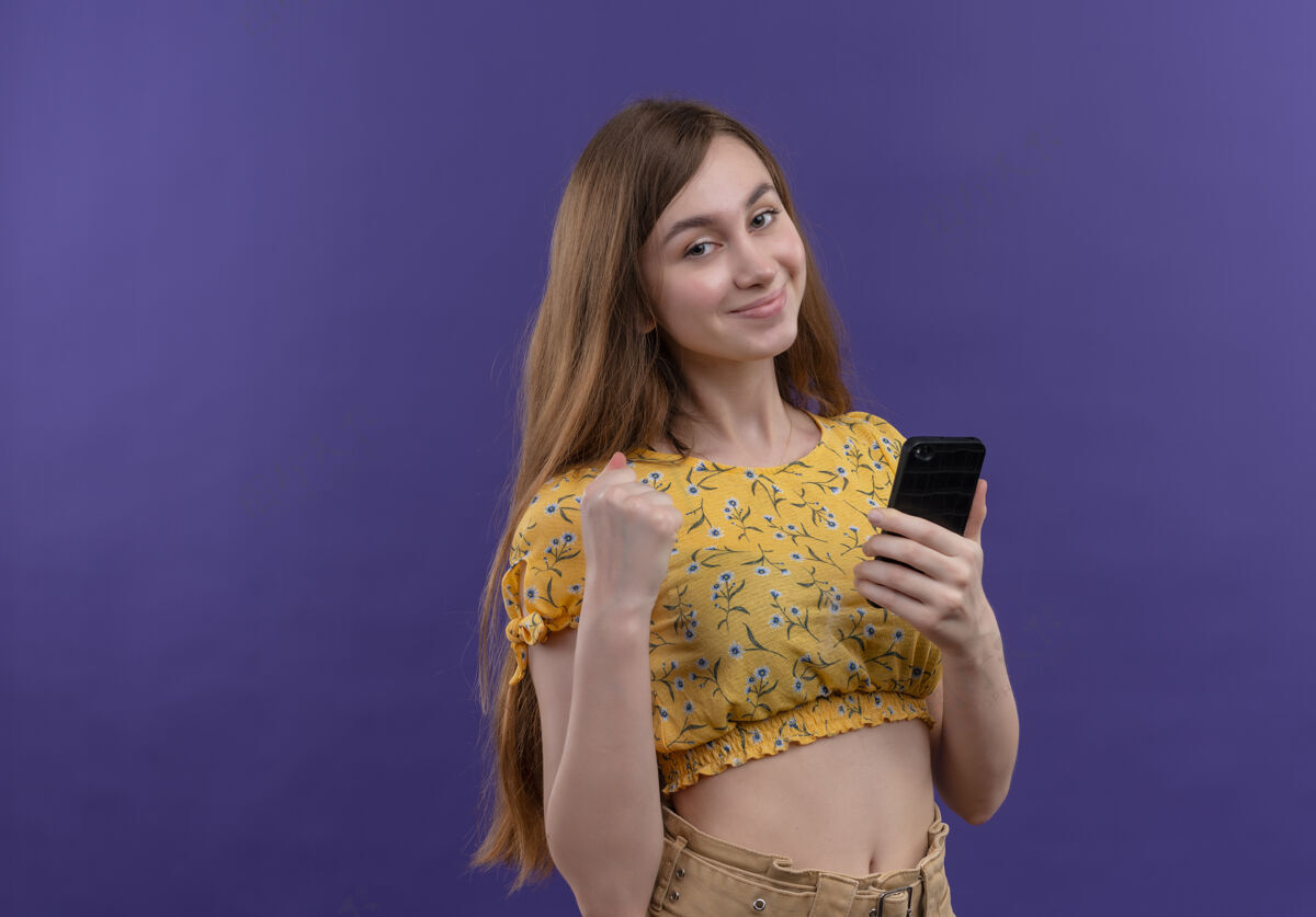 手机自信的年轻女孩握着手机握紧拳头在孤立的紫色空间与复制空间拳头年轻电话