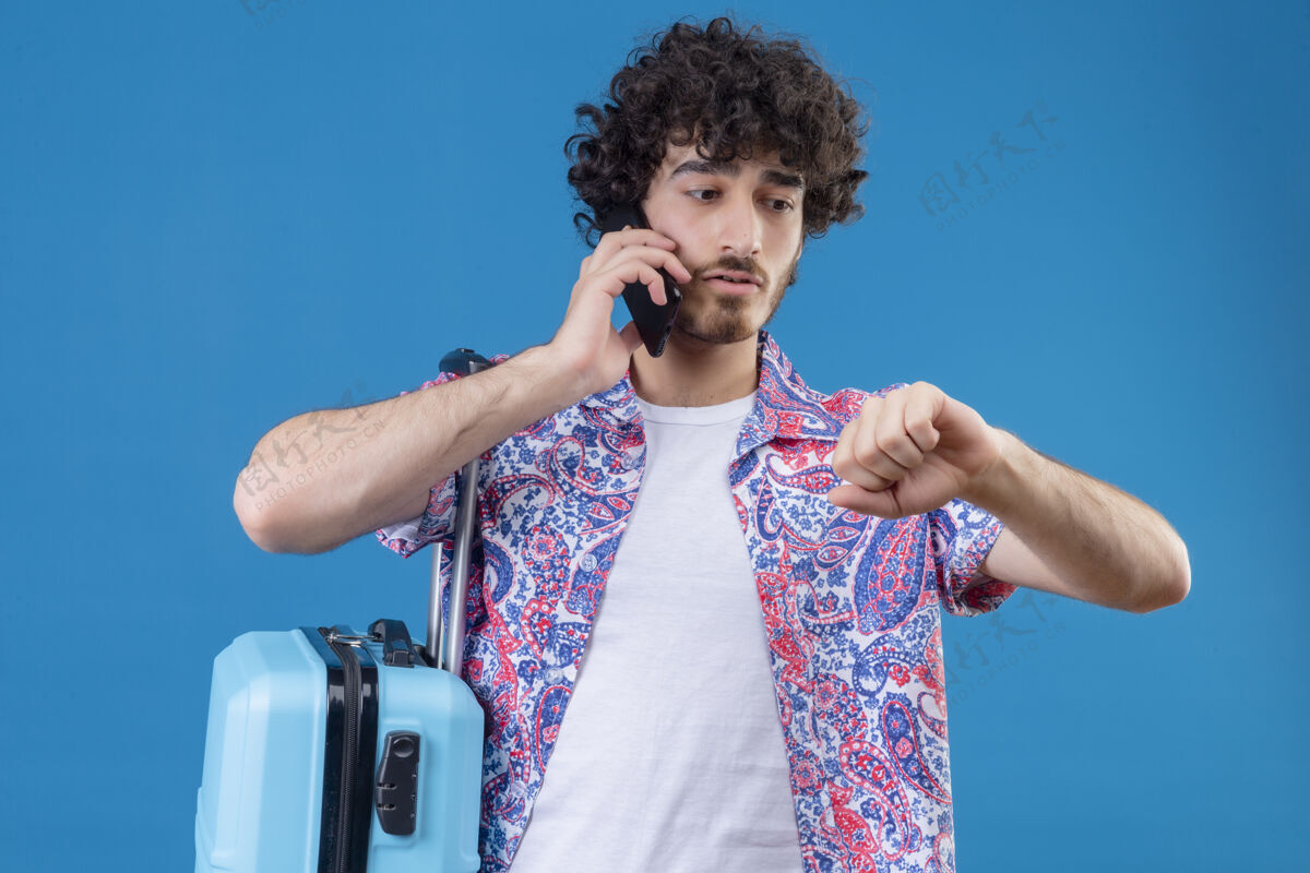 旅行者焦急的年轻英俊的旅行者在电话里握紧拳头看着他手上的手提箱在与世隔绝的蓝色空间拳头英俊手提箱