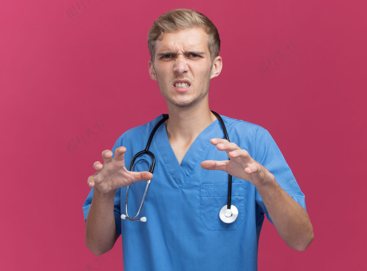 制服愤怒的年轻男医生穿着医生制服 听诊器显示老虎式的手势 隔离在粉红色的墙上人手势公民