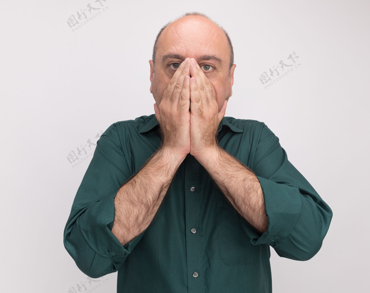 人一位身穿绿色t恤的中年男子脸上蒙着一张脸 双手被隔离在白色的墙上站害怕手