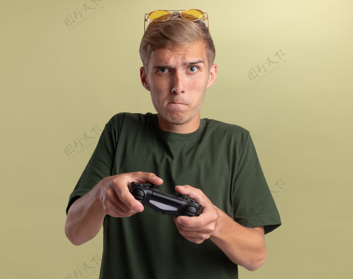帅哥关心的年轻帅哥穿着绿色衬衫 头戴眼镜 在橄榄绿的墙上玩游戏感觉头家伙