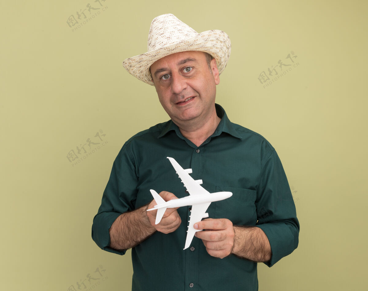 飞机一个穿着绿色t恤 戴着帽子的中年男子 手里拿着玩具飞机 孤零零地站在橄榄绿的墙上衣服穿着人
