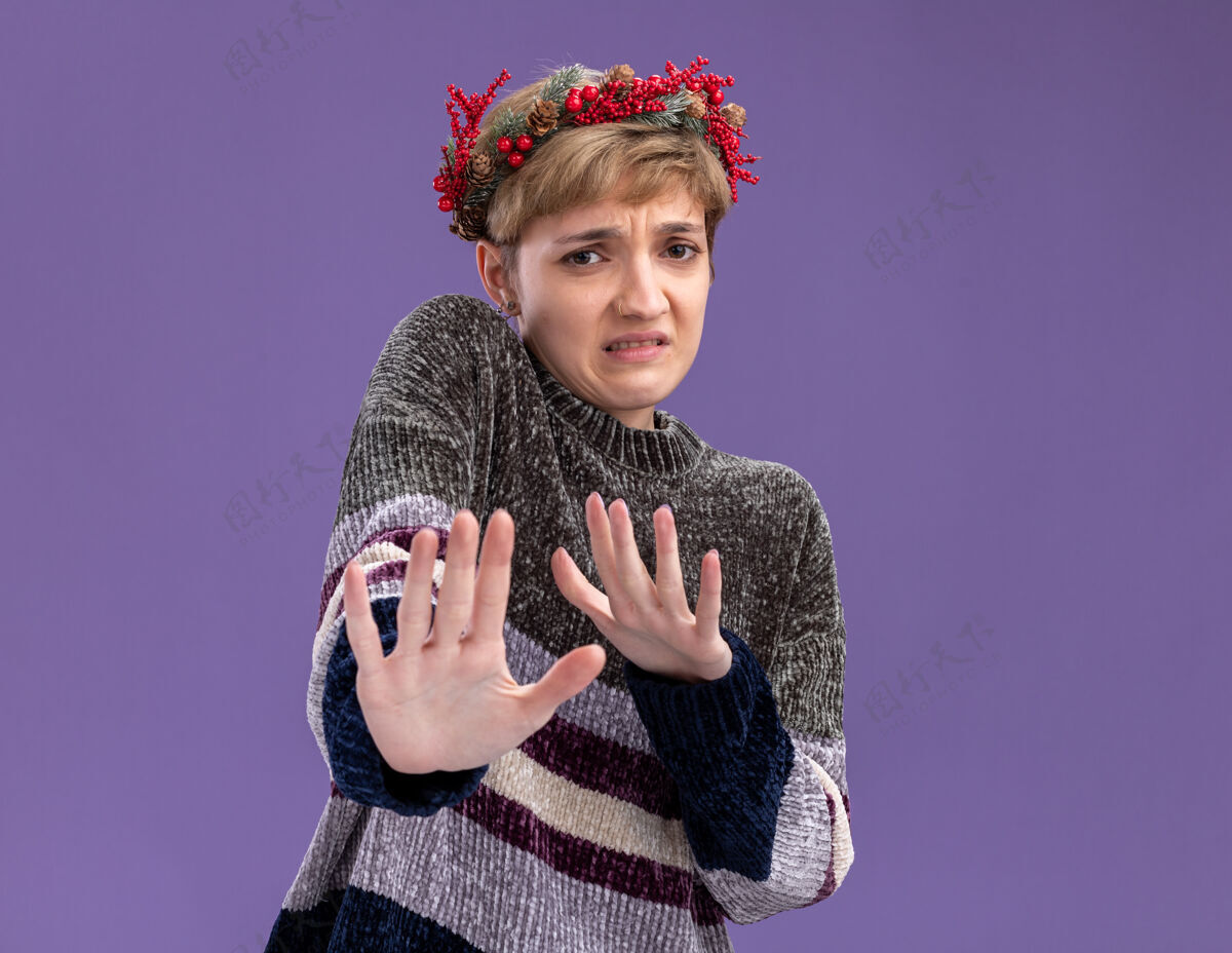 圣诞节恼怒的年轻漂亮女孩戴着圣诞花环看着镜头做拒绝手势孤立在紫色背景上空间拒绝复制