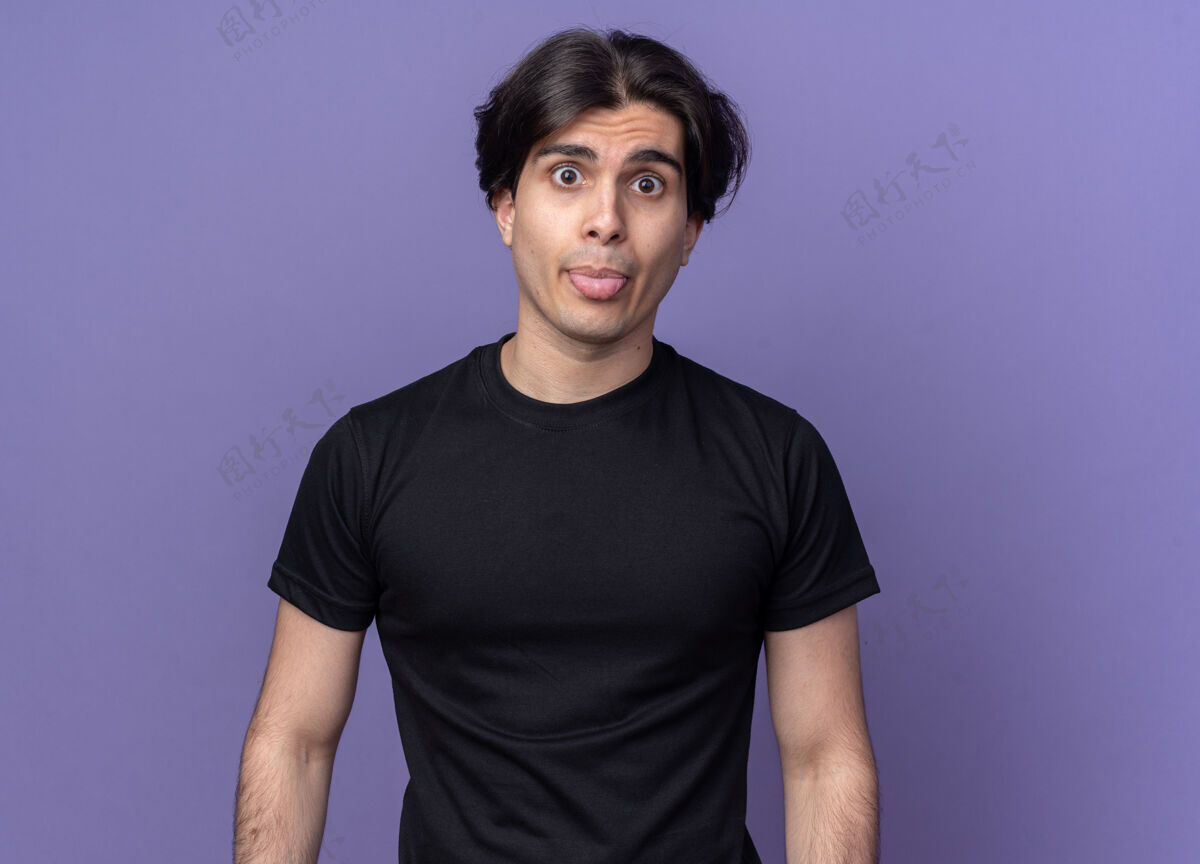 人快乐的年轻帅哥穿着黑色t恤在紫色的墙上露出孤立的舌头人感情表情