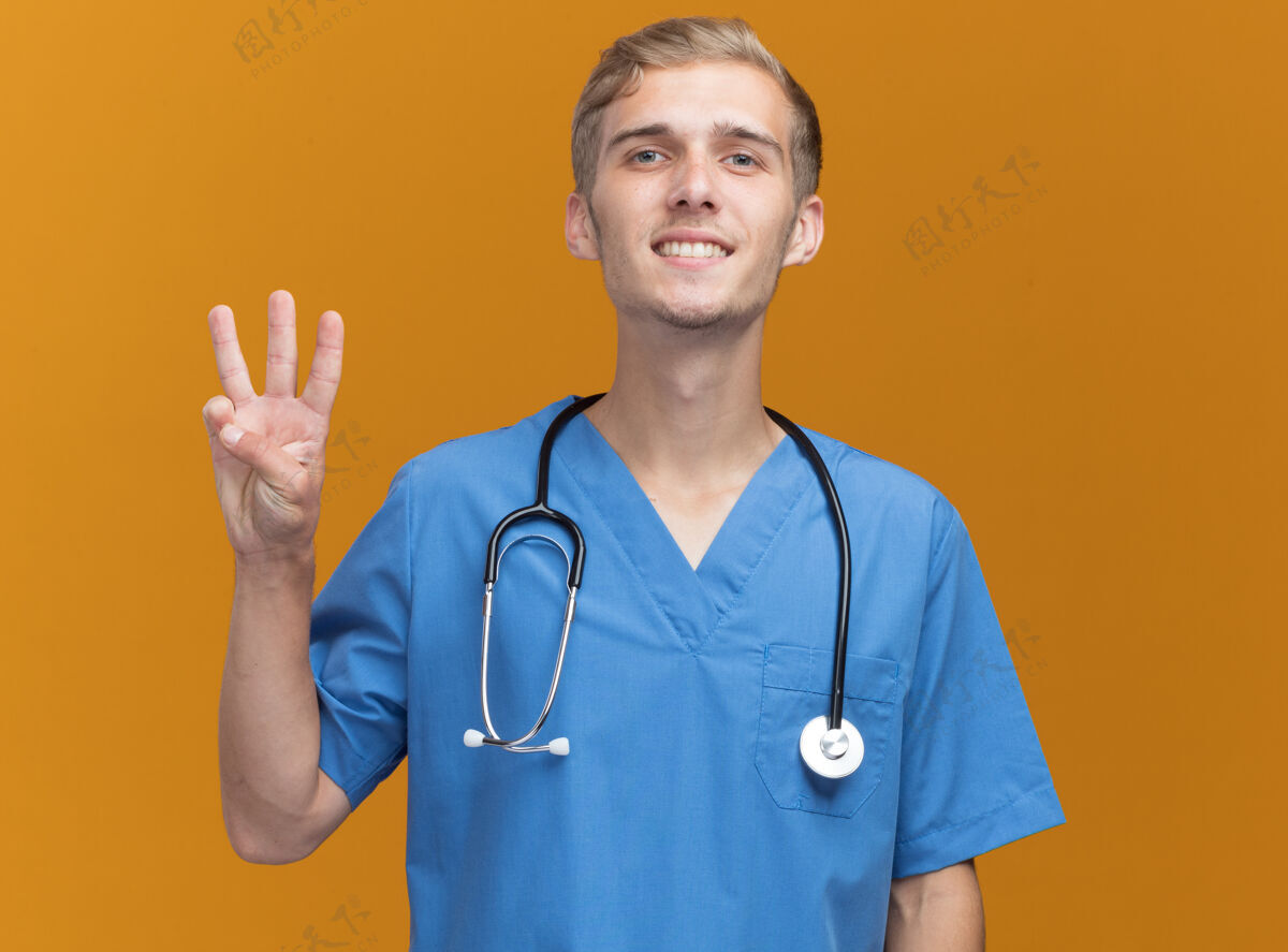 人微笑的年轻男医生穿着医生制服 带听诊器 在橙色的墙上显示三个孤立的人表演站着表情