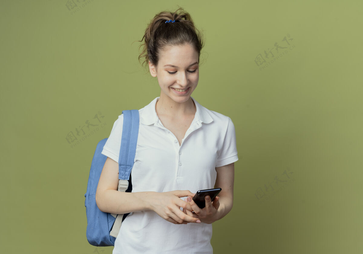 包微笑的年轻漂亮的女学生戴着背袋用手机隔离在绿色背景与复制空间年轻背部漂亮