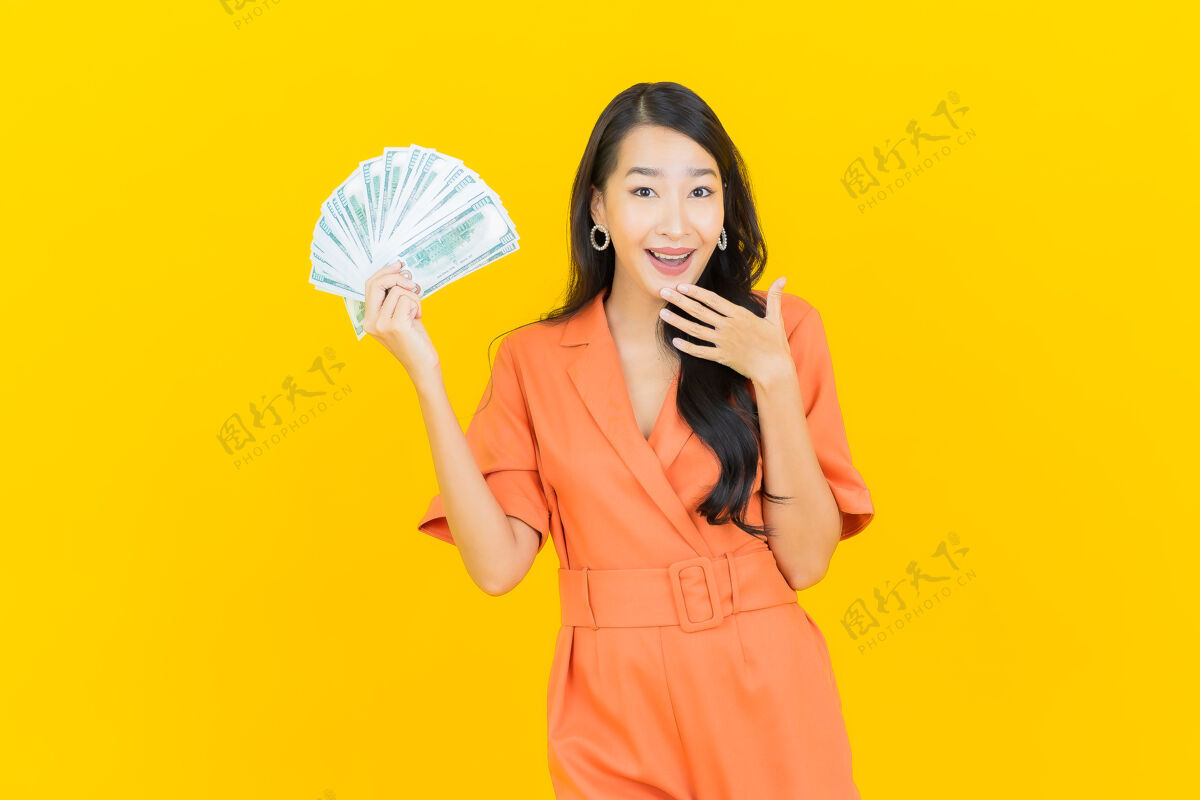 地位肖像美丽的亚洲年轻女子微笑着在黄色上有很多现金和金钱女人财务女士
