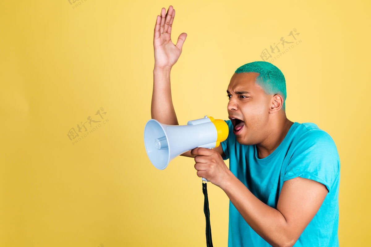 非洲一个穿着休闲装的非洲黑人在黄色的墙上 蓝色的头发在扩音器里尖叫着喊到左边年轻警告扬声器