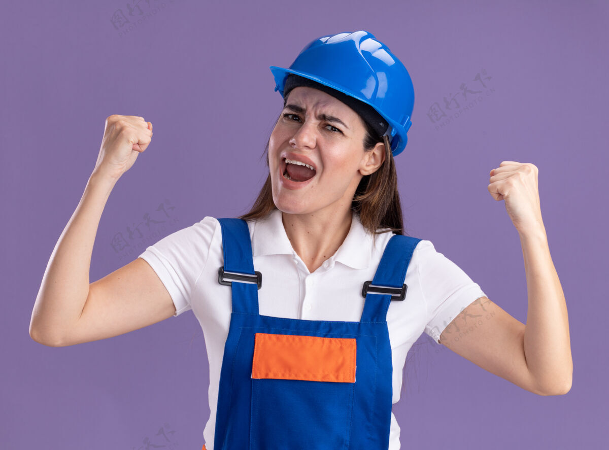 公民身着制服的年轻建筑工人兴奋地在紫色的墙上做着“是”的手势女人建设者年轻人