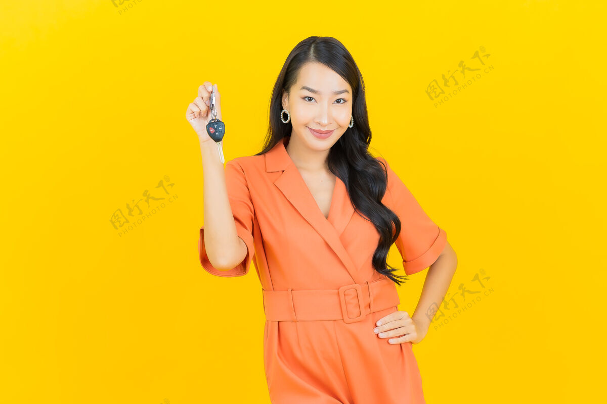 展览肖像美丽的亚洲年轻女子微笑着把车钥匙放在黄色销售购买控股