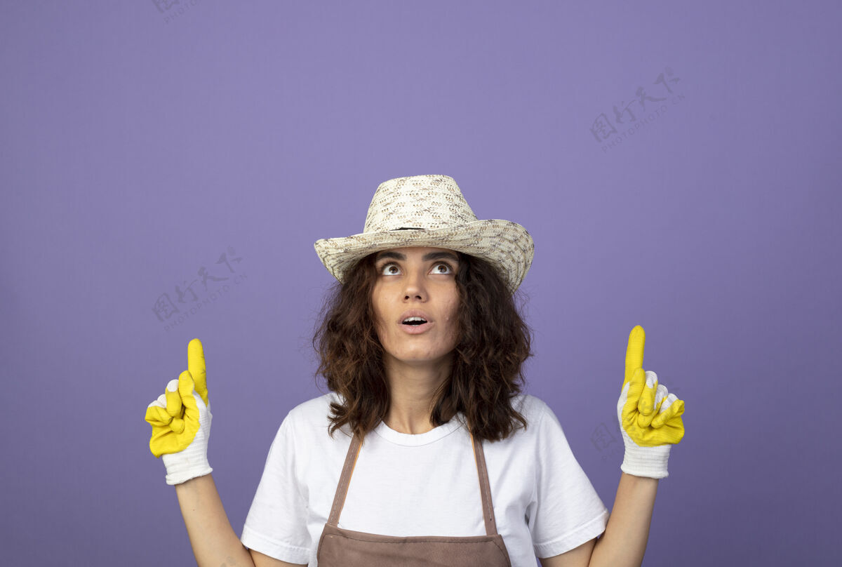 成人印象深刻的年轻女园丁穿着制服 戴着园艺帽子和手套点起来帽子人点