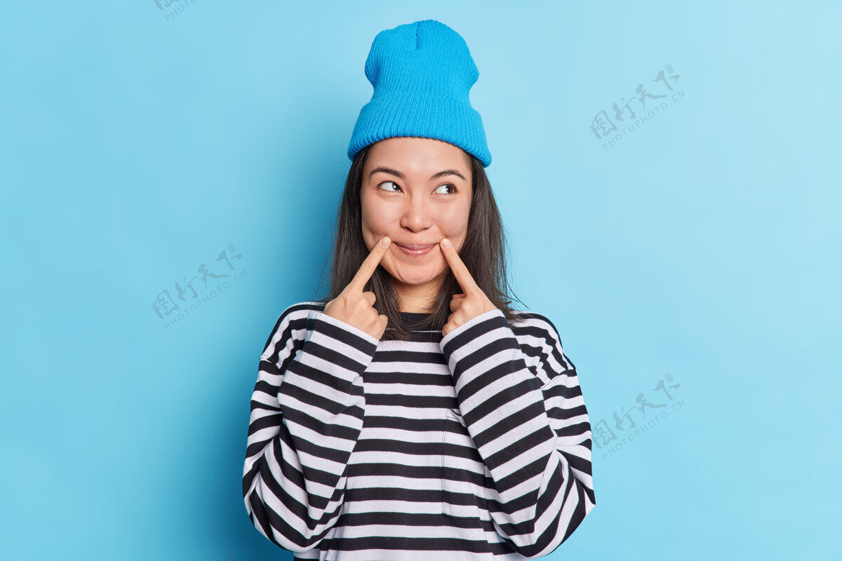 手指深色头发的亚洲女人把手指放在嘴角 脸上露出满意的表情情感年轻乐趣