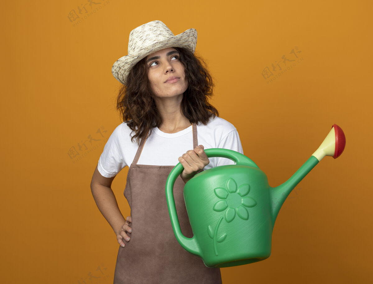 人看着身边穿着制服的年轻女园丁 戴着园艺帽 拿着浇水罐 手放在屁股上园艺年轻制服