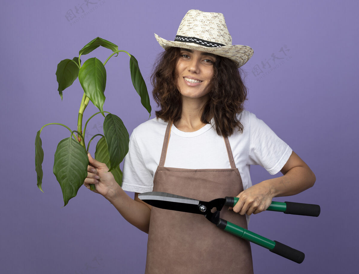 穿年轻的女园丁面带微笑 穿着制服 戴着园艺帽 手里拿着剪子成人花园女人