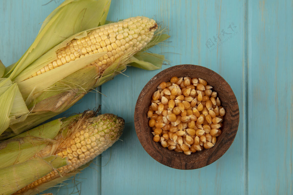 顶部蓝色木桌上的木碗上 有机健康的玉米 头发和玉米粒的俯视图木头碗玉米