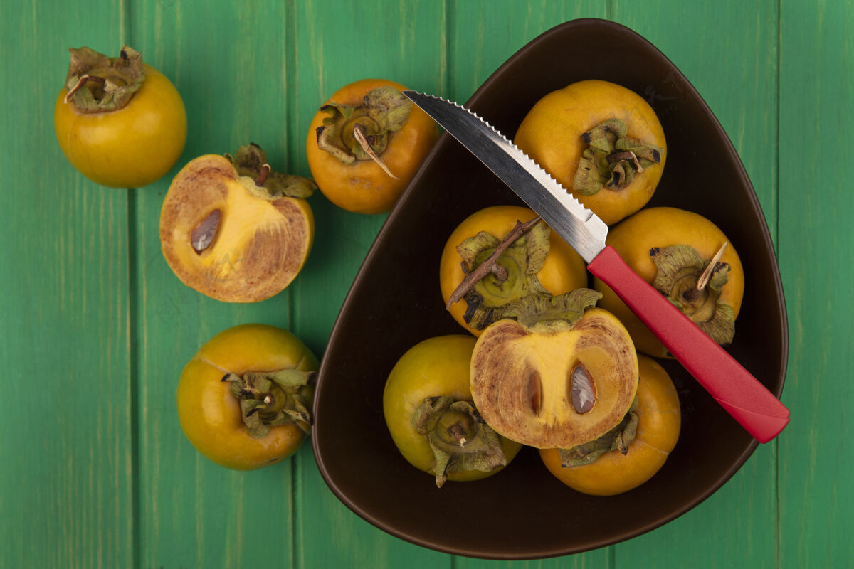 食物新鲜柿子水果的顶视图在一个绿色的木桌上用刀放在一个碗里碗绿色木头