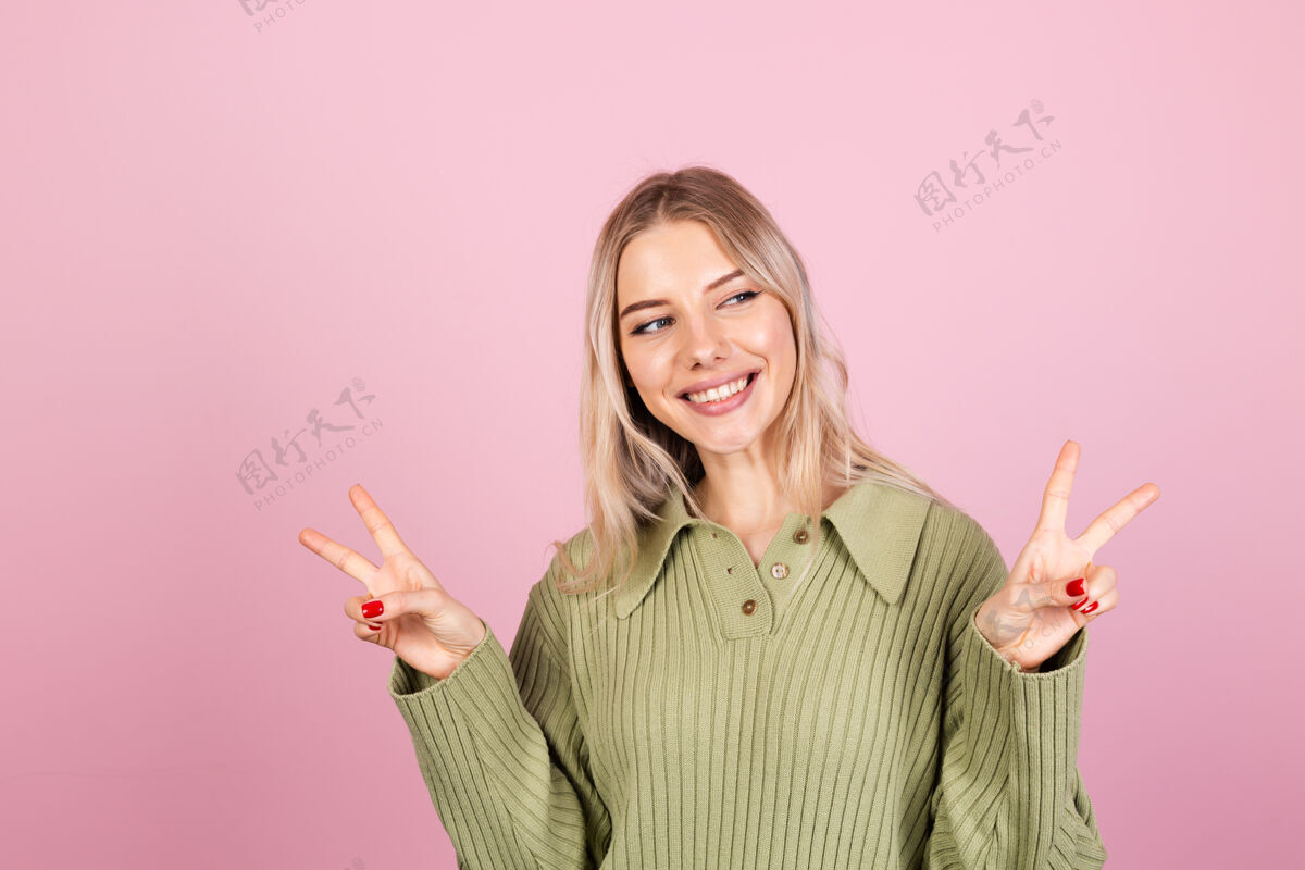 表情粉色墙上穿着休闲毛衣的漂亮欧洲女人情感学生手指