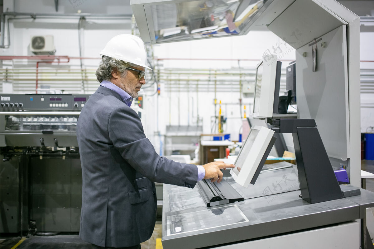 机器专注于男性工厂经理操作工业机器 按下控制面板上的按钮成熟安全帽操作