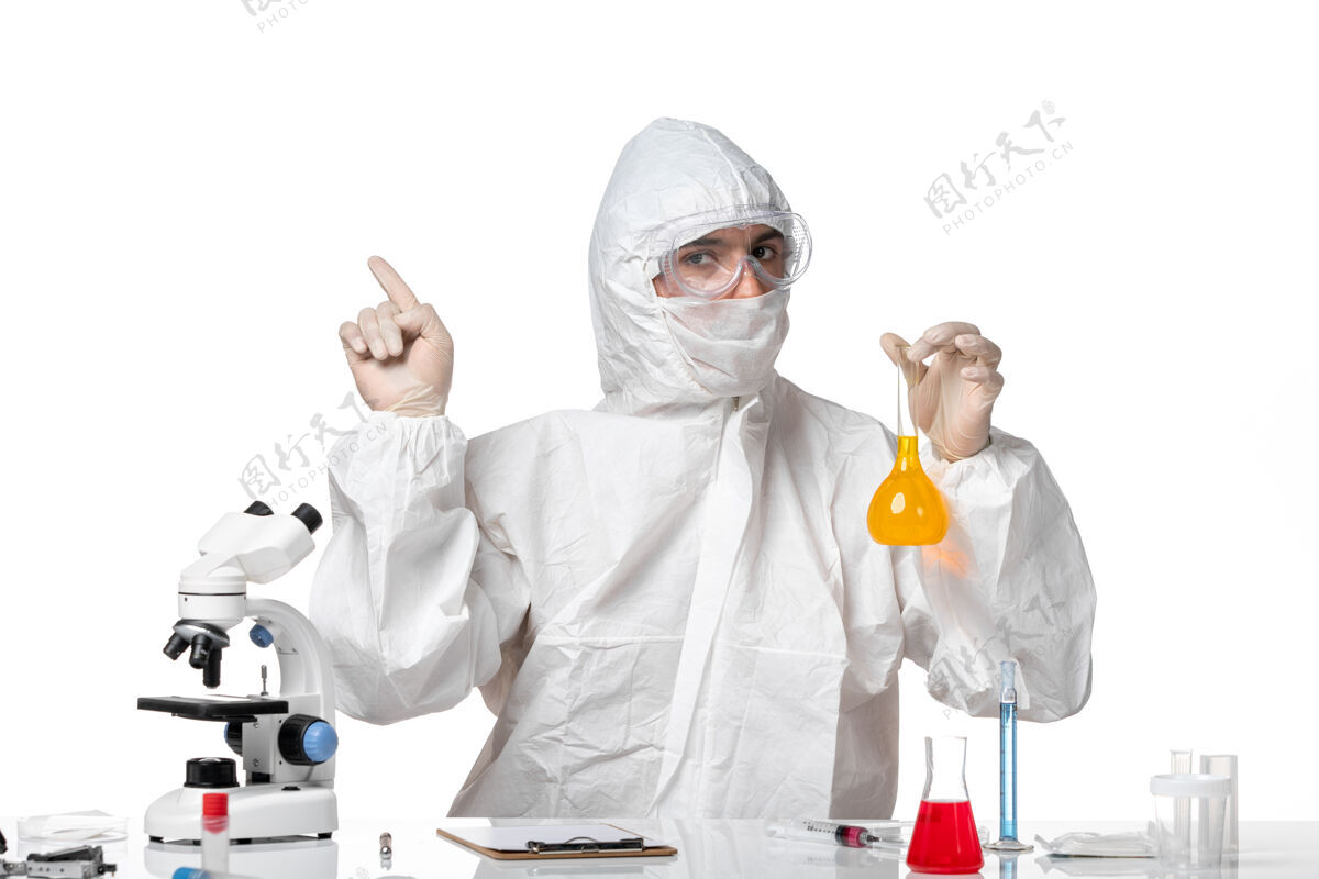 视图正面图：男医生穿着防护服 戴着面罩 因为白色空间上有一个装有黄色溶液的瓶子烧瓶药品医生