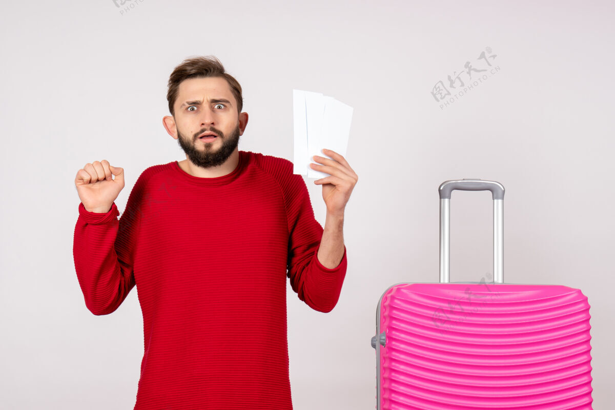 游客正面图：年轻男性 带着粉色包 手持白墙上的机票 远航彩色旅游度假照片年轻男性颜色漂亮