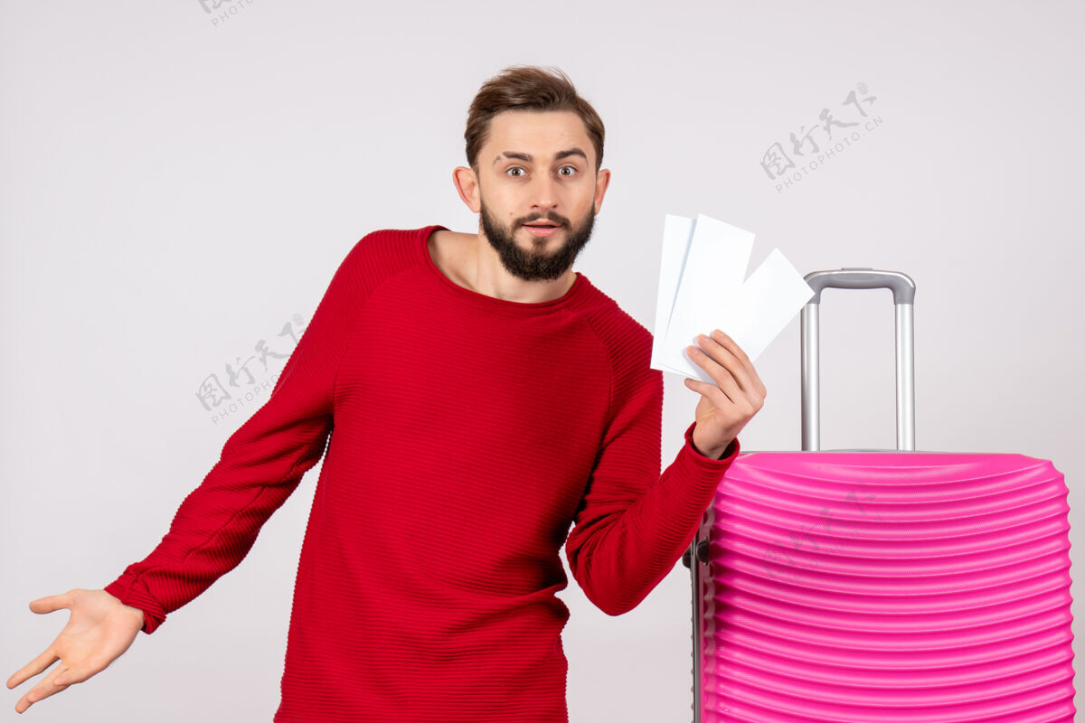 颜色正面图年轻男子带着粉红色的包 拿着白墙上的彩色旅行票度假旅游成人男人机票