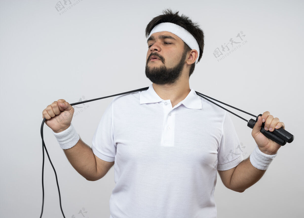运动自信的年轻运动型男人看着戴着头带和手环的侧面 脖子后面拿着大绳 隔离在白墙上年轻脖子信心