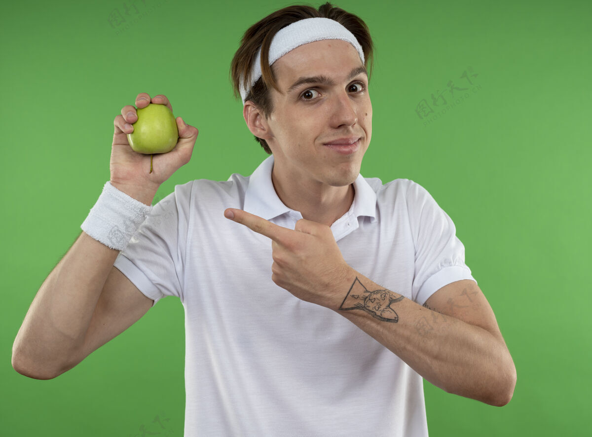 举行高兴的年轻人戴着头带与腕带举行 并在绿色的隔离墙苹果点运动运动年轻穿