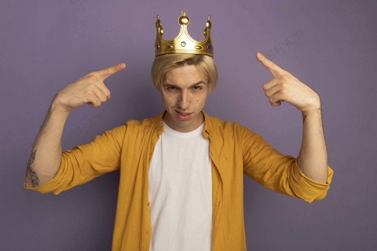 金发穿着黄色t恤和皇冠的自信的金发小伙子指着自己被紫色隔离自己穿皇冠