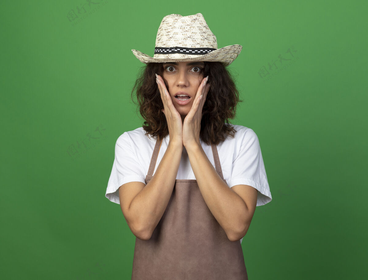 年轻年轻的女园丁穿着制服 戴着园艺帽 手放在脸颊上 吓了一跳人女人帽子