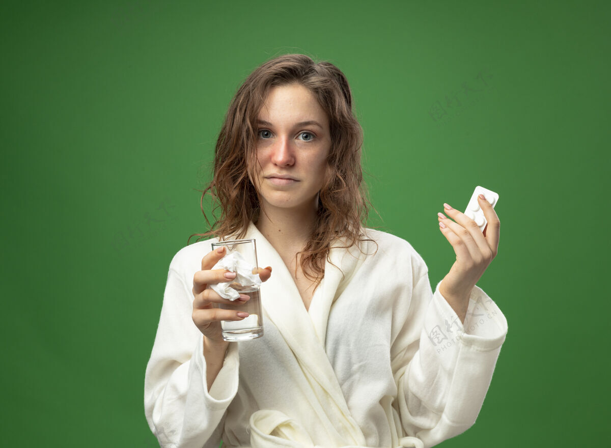 水高兴的年轻病女孩直直地看着前面穿着白色长袍拿着一杯水与药丸隔离在绿色穿药丸持有