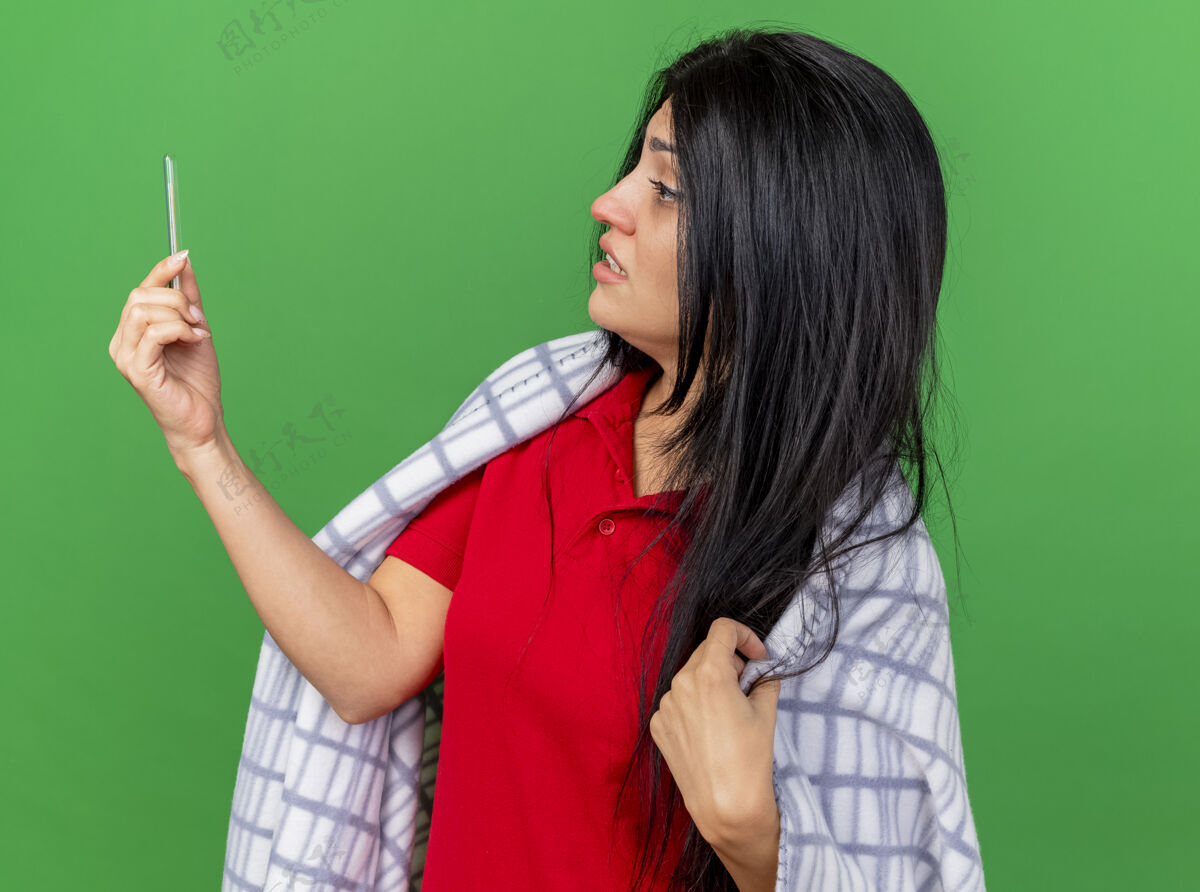 感觉焦急的年轻病妇裹着格子布 手里拿着温度计 看着隔离在绿墙上的格子布人抱着衣服
