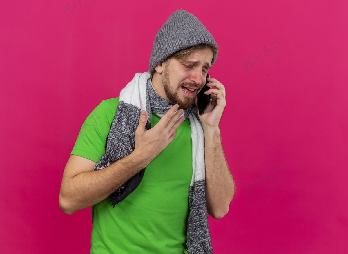 空气年轻英俊的斯拉夫病夫戴着冬天的帽子 戴着围巾打电话 手举在空中 闭着眼睛 隔离在粉红色的墙上 留着复印空间围巾眼睛帽子