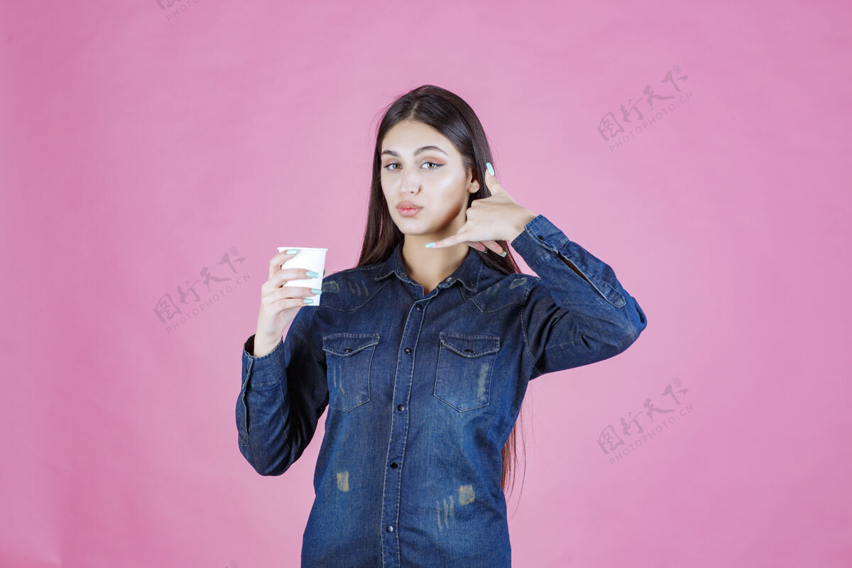 符号穿着牛仔衫的女孩拿着咖啡杯 打着呼号女人人调情