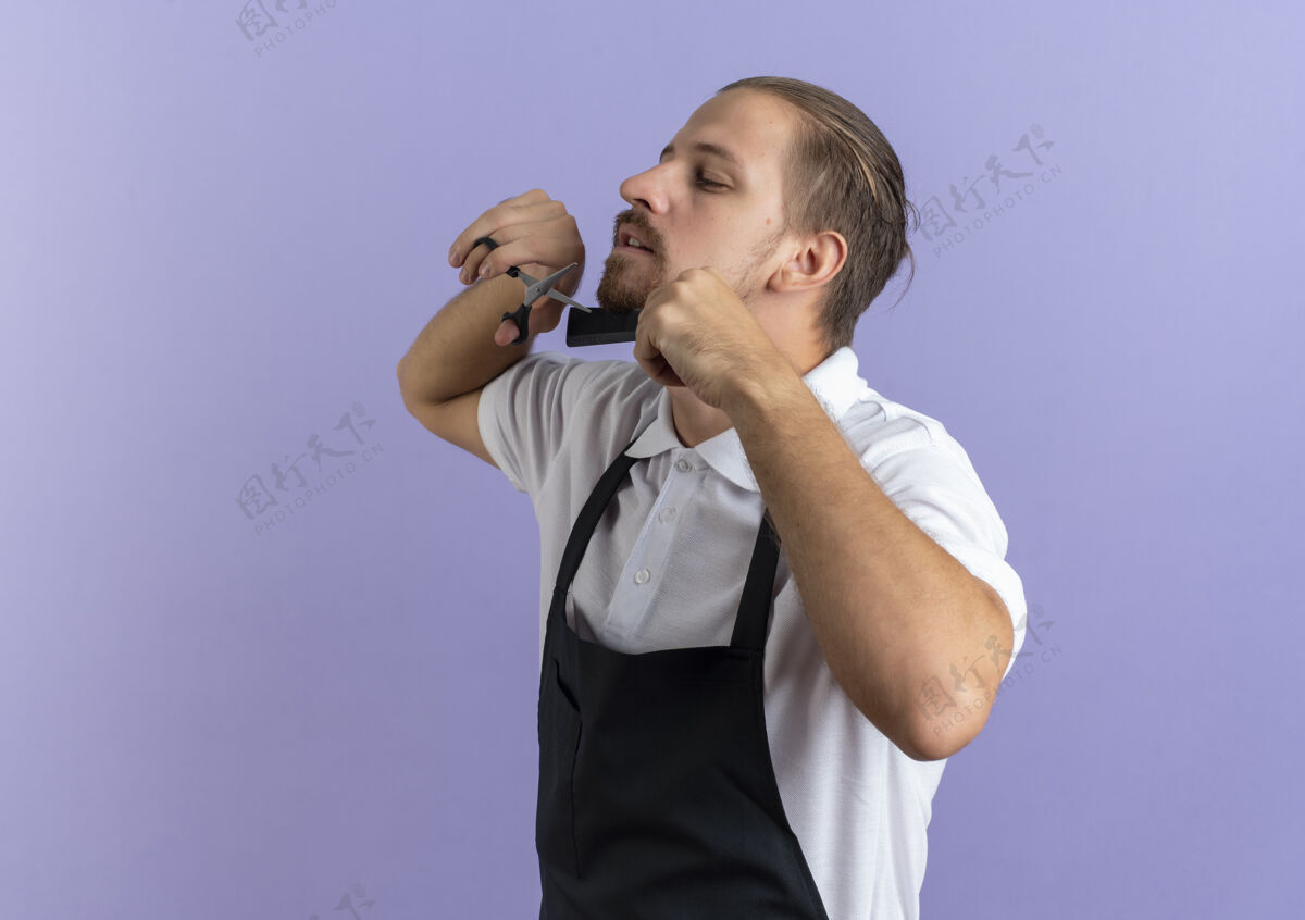 理发师年轻帅气的理发师穿着制服 梳着自己剪的胡子 隔离在紫色的背景上 留着复制空间年轻胡须帅气