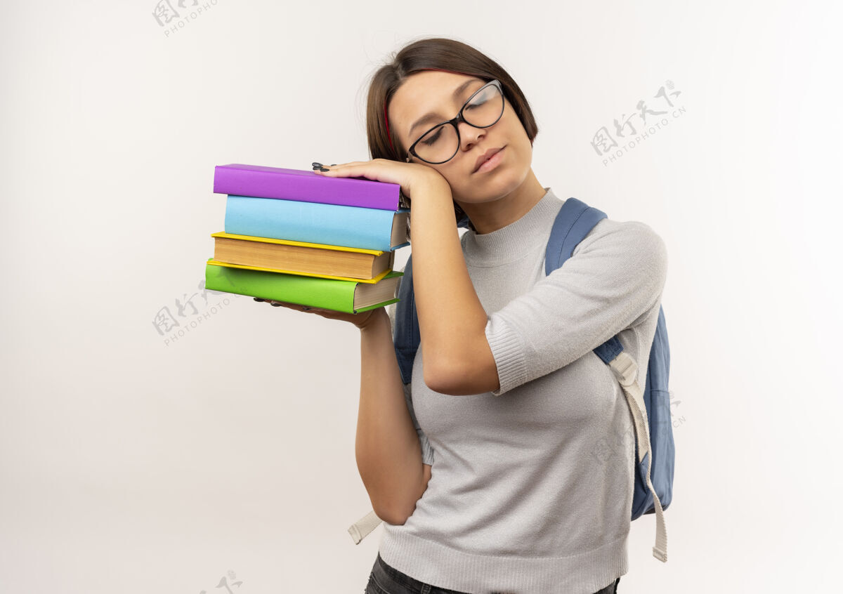 头疲惫的年轻女学生戴着眼镜 背着书包拿着书 把头靠在书上 试图在白色的背景下独自入睡试试学生女孩
