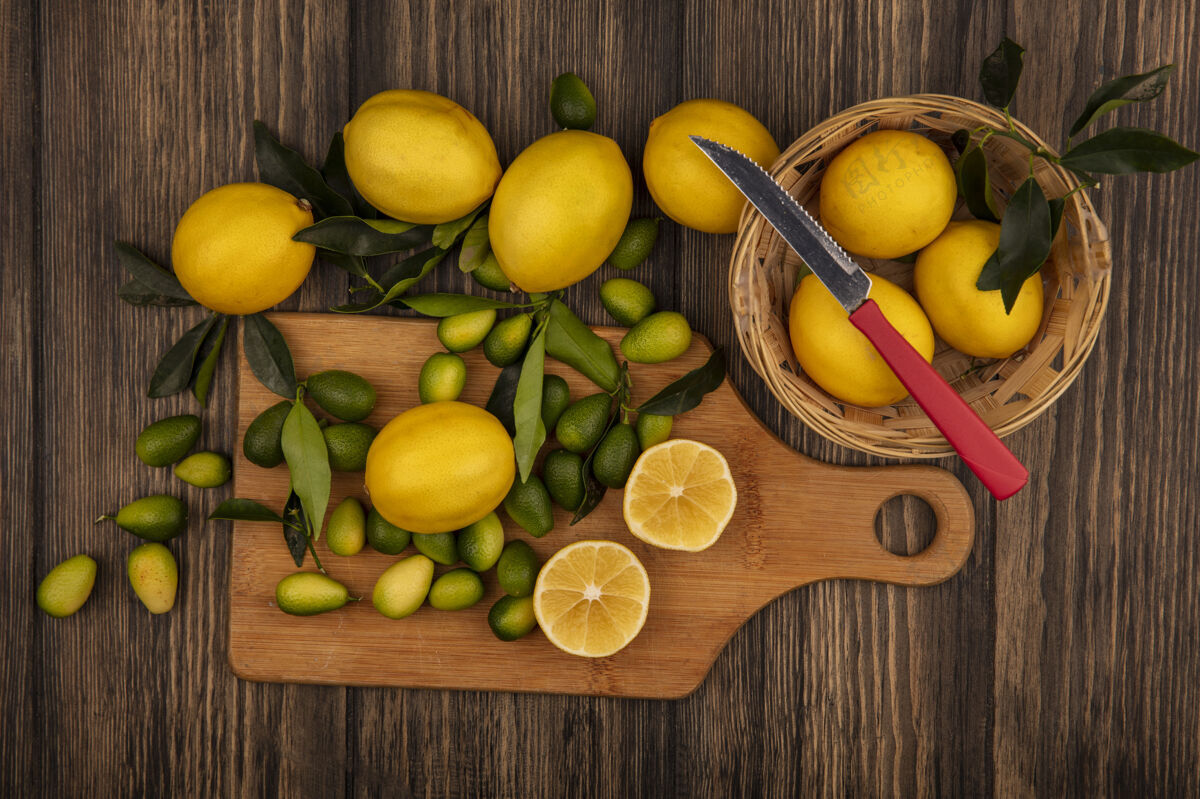 顶部一个桶上新鲜的黄色柠檬的俯视图 在木制背景上的木制厨房板上有一把带有柠檬和金盏花的刀柠檬刀柑橘
