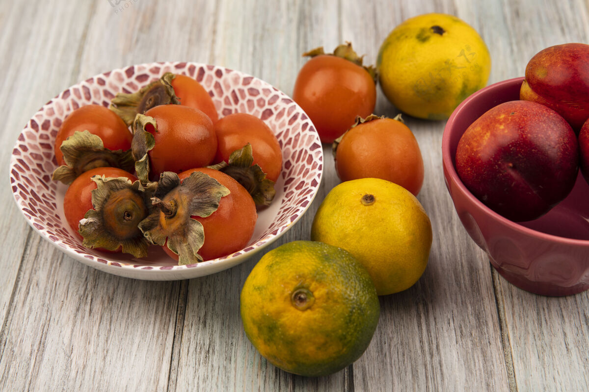 碗在灰色的木制背景上 一个碗里盛着柿子和橘子的多汁桃子的俯视图食物观点桃
