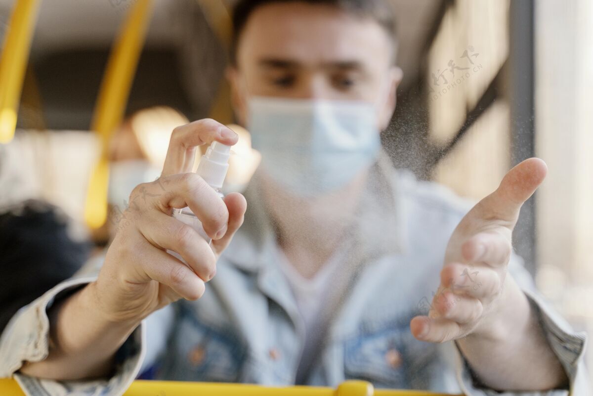 城市公共汽车坐城市公共汽车旅行的年轻人用消毒剂凝胶给他的手消毒外科口罩感染预防交通