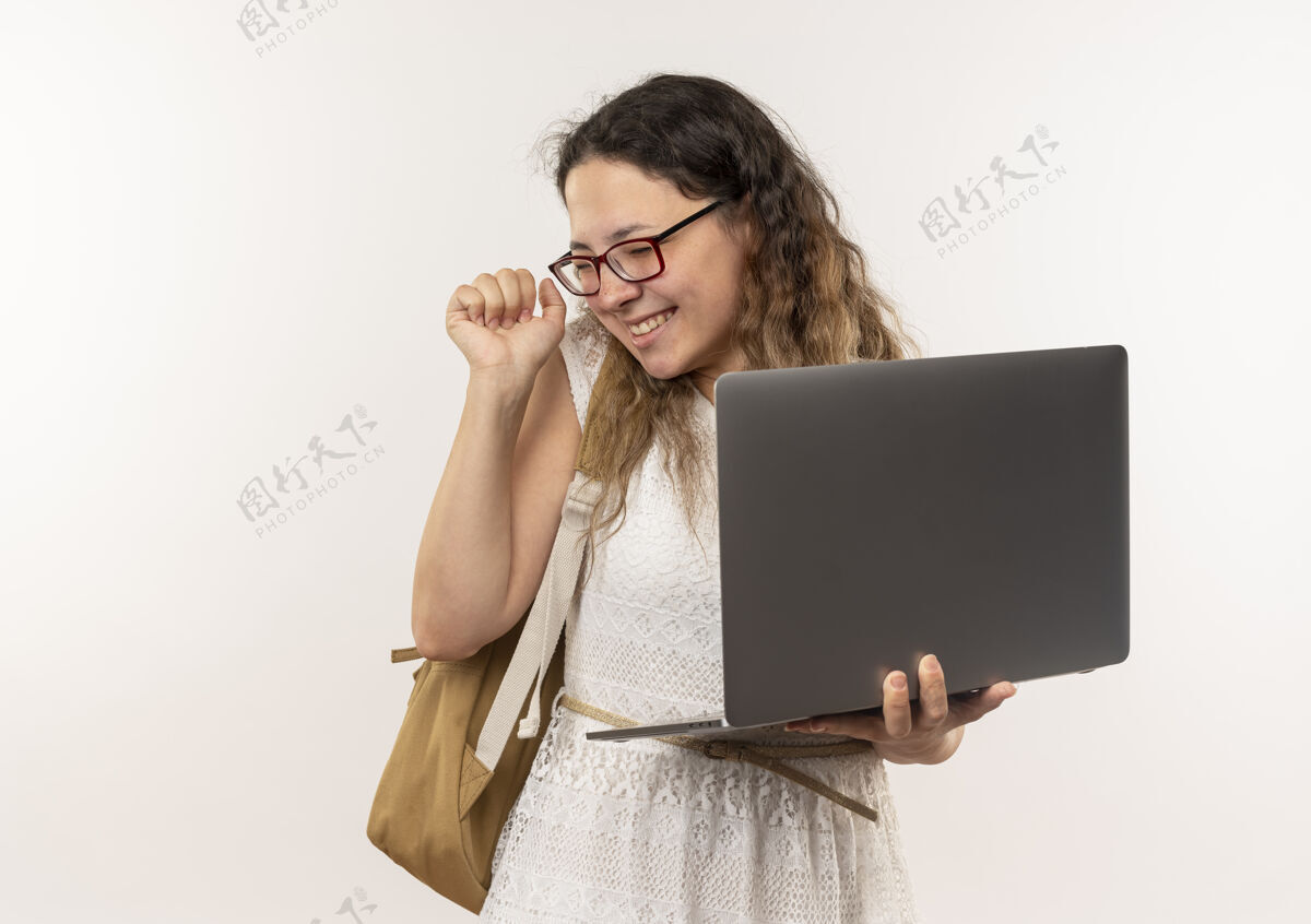 关闭快乐的年轻漂亮的女学生戴着眼镜 背着书包 拿着笔记本电脑 紧握拳头 闭着眼睛穿年轻举行