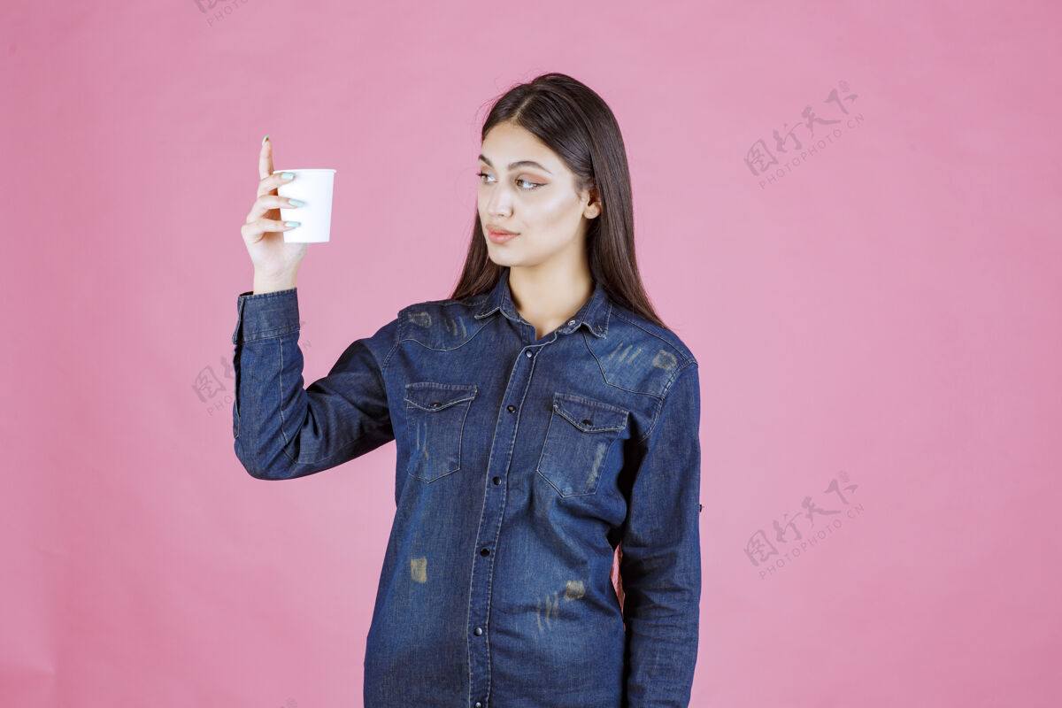 温暖穿着牛仔衬衫的女孩手里拿着一个咖啡杯 看上去若有所思 疑神疑鬼成人女性思考