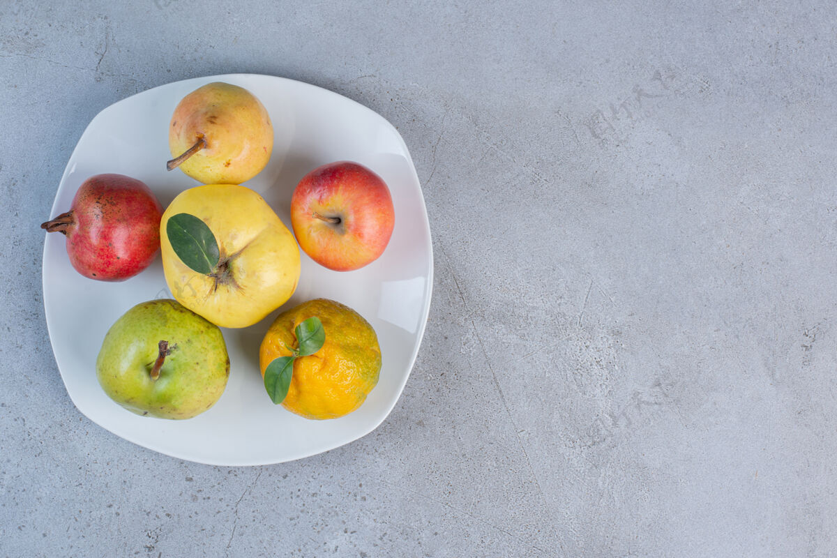 营养把石榴 梨 橘子 木瓜和苹果放在大理石背景的盘子里新鲜石榴美味