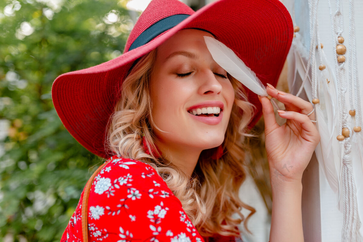 脸近距离肖像迷人时尚金发微笑的妇女在稻草红色帽子和衬衫夏季时尚服装举行白色羽毛性感性感的面部皮肤配饰牙齿华丽