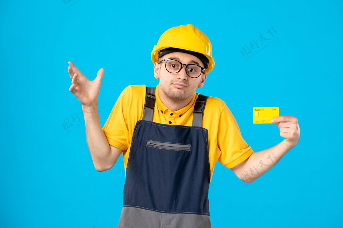 男性蓝色墙壁上穿着制服 带信用卡的男建筑工人的正视图建筑工人专业前面
