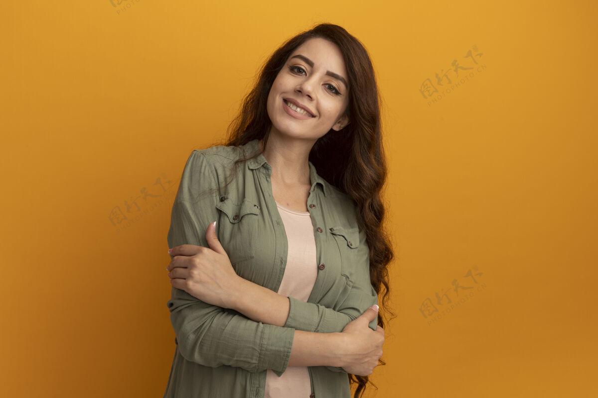 橄榄微笑的年轻漂亮女孩穿着橄榄绿t恤双手交叉隔离在黄色的墙上微笑年轻交叉